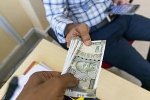 Osoba odovzdáva 500-roupí indickú bankovku inej osobe.