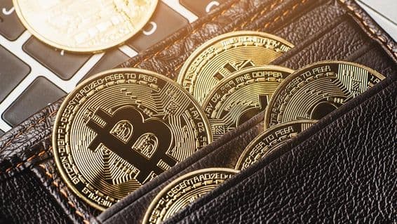 Bitcoin mince v koženom peňaženke na klávesnici počítača.