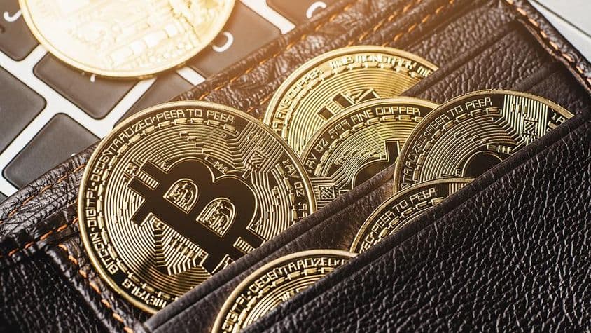 Bitcoin mince v koženom peňaženke na klávesnici počítača.