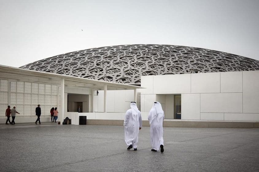 Turisti v múzeu Louvre Abú Dhabí a dvaja ľudia v bielom tradičnom emirátskom oblečení.