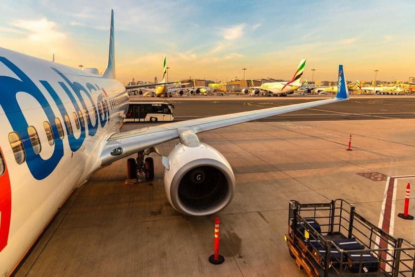 Lietadlo flydubai zaparkované s viacerými ďalšími lietadlami v pozadí a autobus pre pasažierov, vpravo s batožinou na malom dopravnom vozidle.