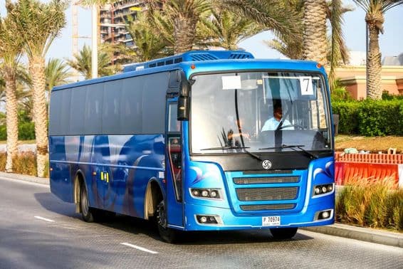 Modrý autobus v Dubaji s palmami v pozadí.