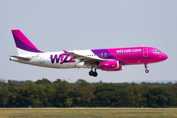 Lietadlo Wizz Air letiace v nízkej výške s lesom v pozadí.