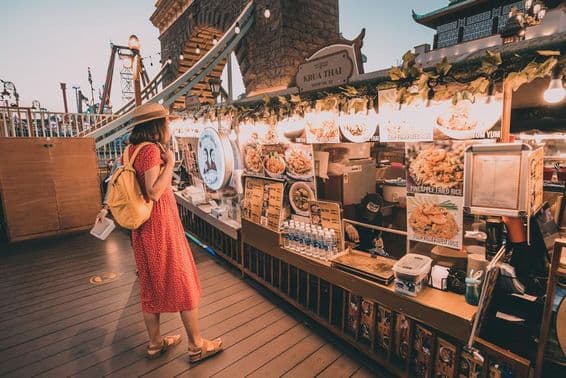 Žena v červených šatách s bodkami obzerajúca národné kuchyne v Global Village, Dubaj.