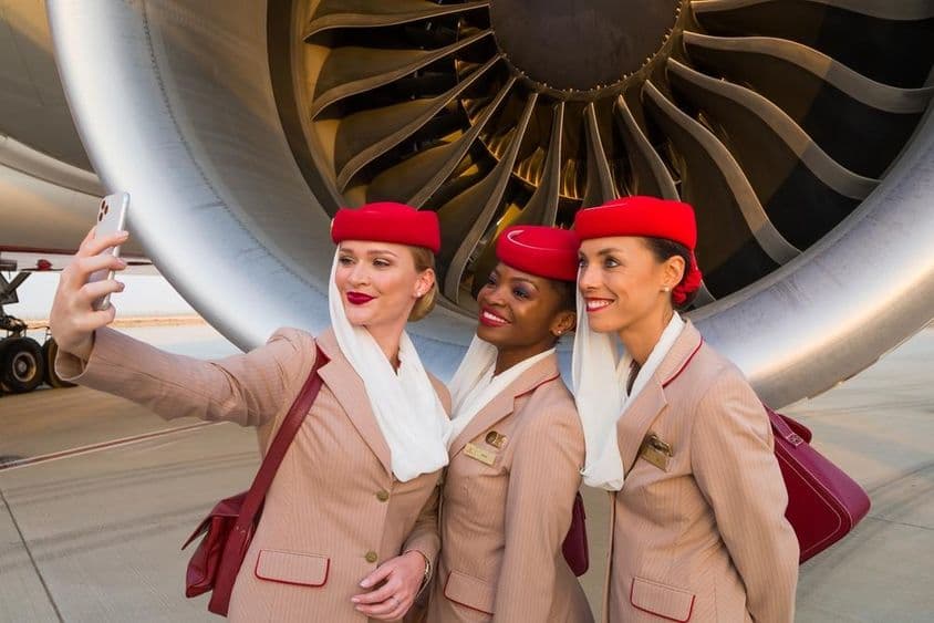 Traja letušky Emirates si robia selfie pred motorom lietadla Emirates.