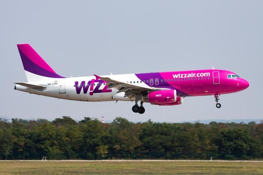 Lietadlo Wizz Air letí v nízkej výške, v pozadí les.