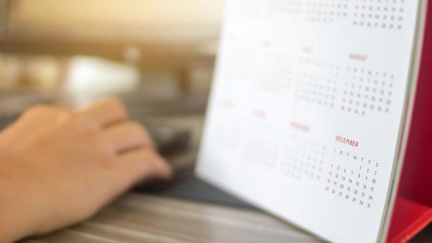 Ruka vedľa kalendára s rozostrenými mesiacmi a s jasne viditeľným decembrom.