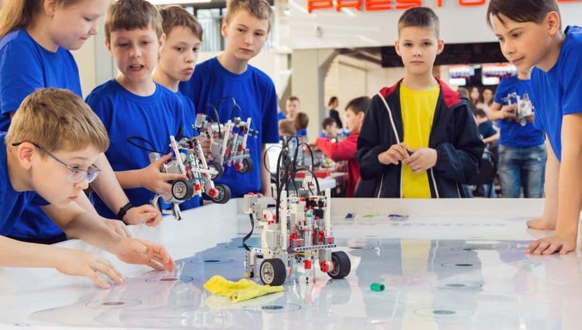 Študenti v modrých tričkách stavajú a programujú robota.