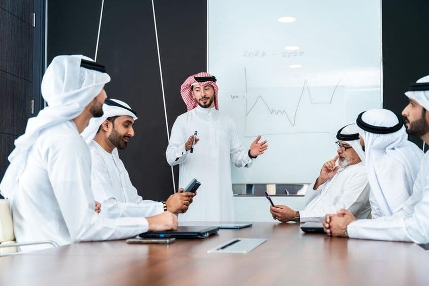 Arabskí dizajnéri diskutujú pred tabuľou, s poznámkovým blokom a telefónom na stole.
