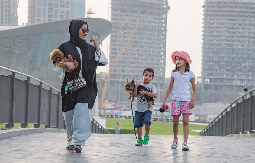 Rodina štyroch pred dubajskými mrakodrapmi, s matkou a jedným dieťaťom držiacim psa.