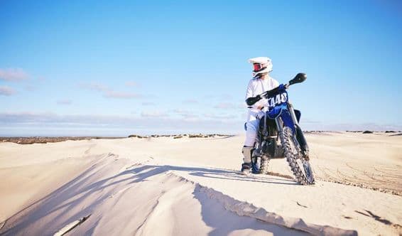 Osoba na motocykli v púšti, oblečená v bielom na modrom motocykli.