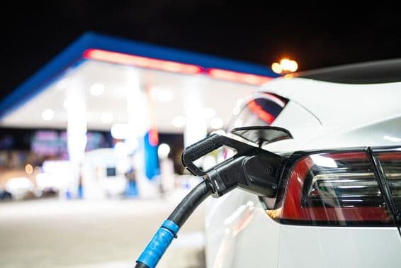 Tesla je nabíjaná, v pozadí s čerpacou stanicou.