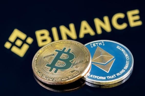 Nápis Binance v pozadí na čiernom stole s Bitcoin a Ethereum mincou.