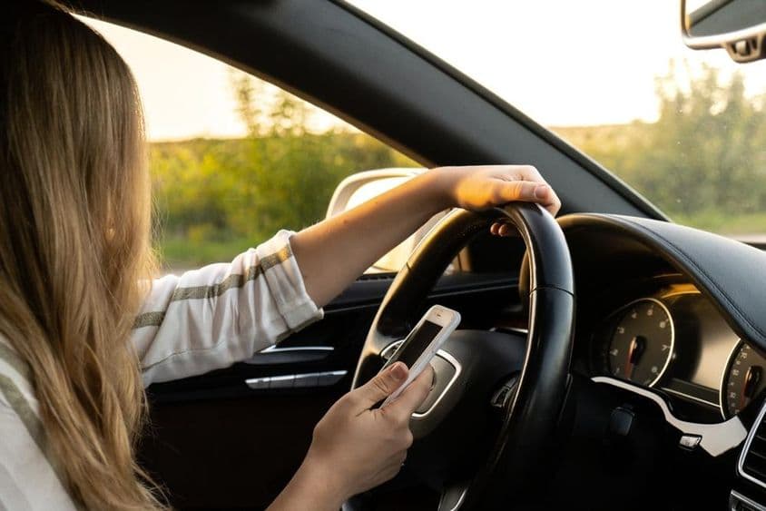 Žena používa mobilný telefón počas jazdy, jednou rukou drží volant.