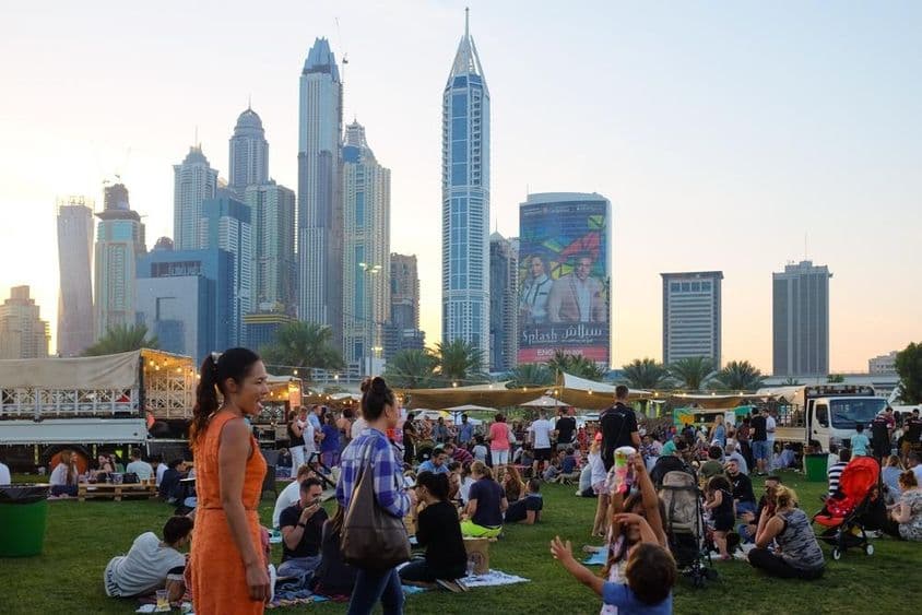 Ľudia v Dubaji sedia v parku, mrakodrapy v pozadí.