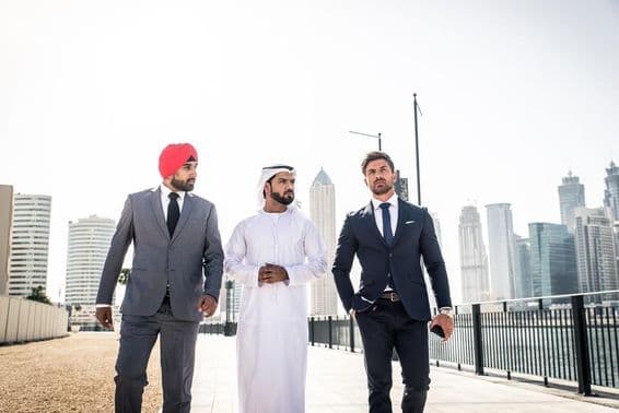 Ind, Emiráčan a Európan kráčajúci popri kanáli, mrakodrapy za nimi.