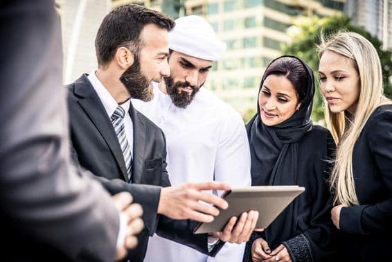 Európan a Emirátsky muž s tabletom, obklopený blondínkou a Emirátkou, sledujúcí