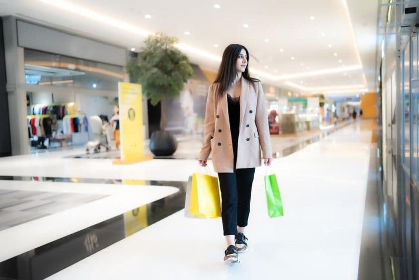 Žena nakupuje v Dubai Mall, držiaca dve tašky, obchody v pozadí.