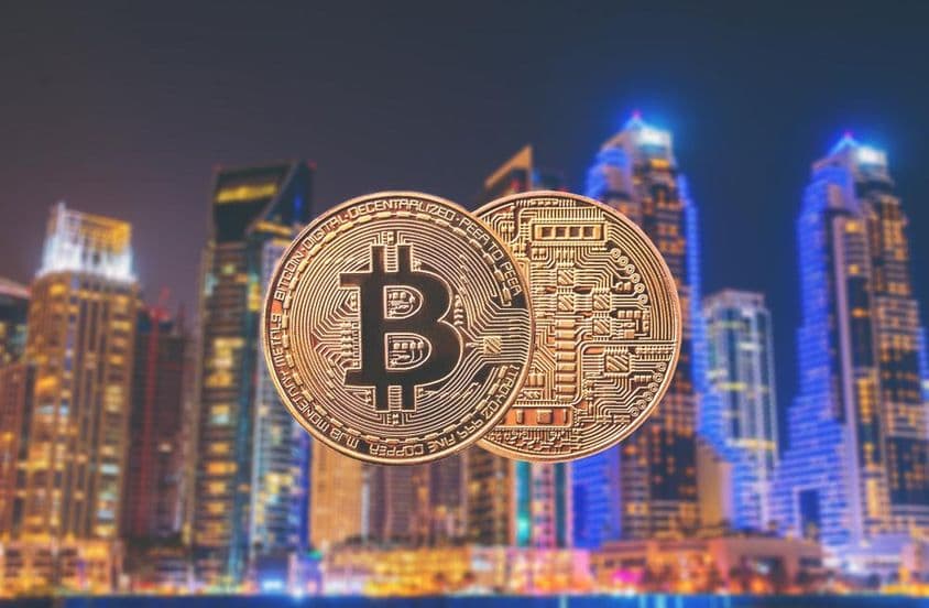 Bitcoin mince v popredí s mrakodrapmi v pozadí.