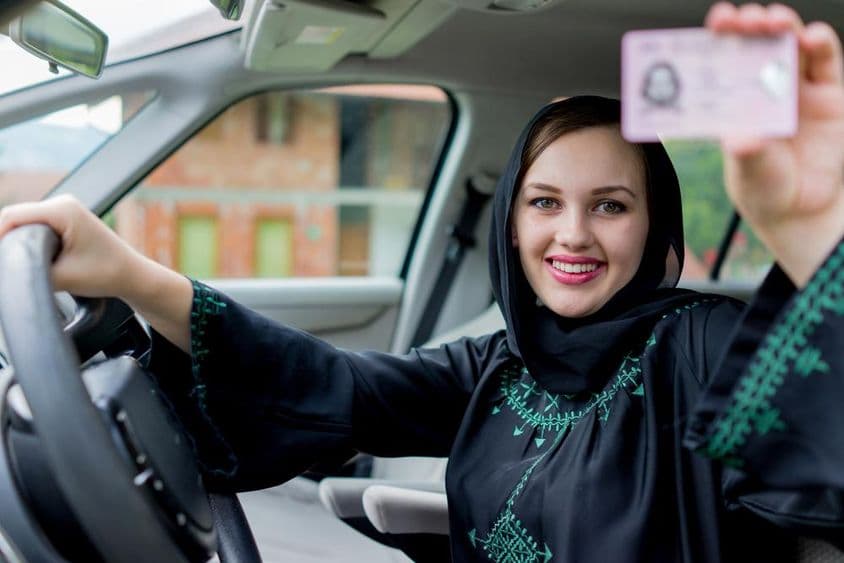Dáma v Dubaji drží vodičský preukaz jednou rukou a volant druhou, usmievajúca sa.