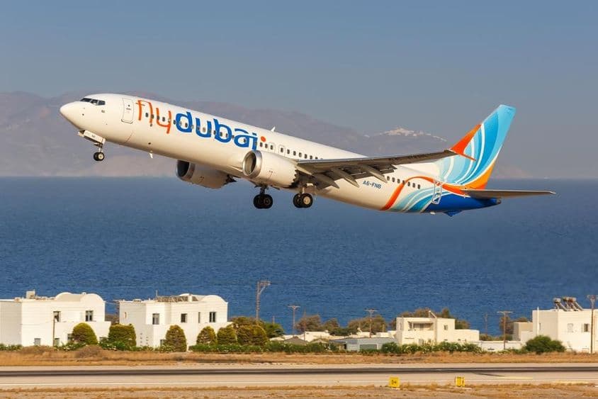 lietadlo flydubai letiace v malej výške, s malými bielymi domami a morom v pozadí.