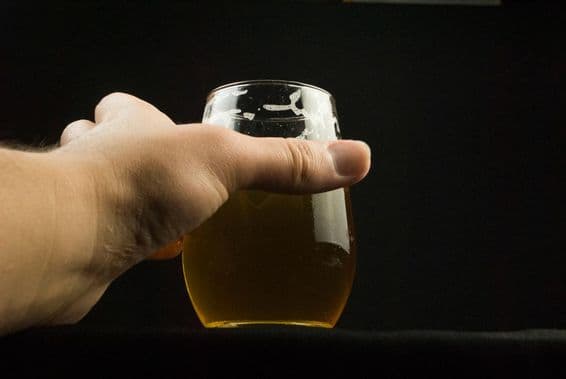 Ruka držiaca pohár s pivom, viditeľná len ruka a pohár.