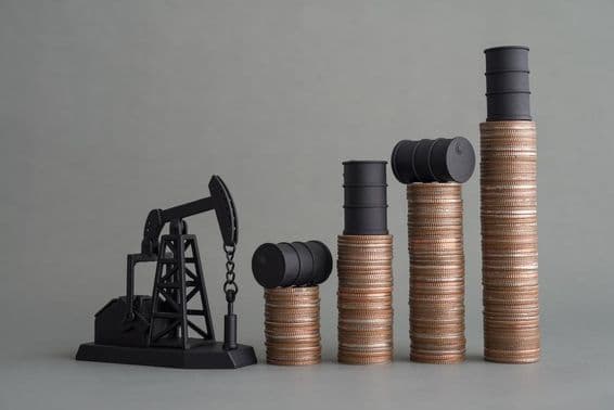 Miniatúrna vrtná veža a naskladané mince s ropným barelom navrchu.