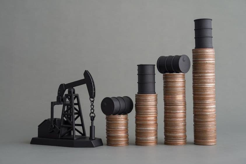 Miniatúrna vrtná veža a naskladané mince s ropným barelom navrchu.