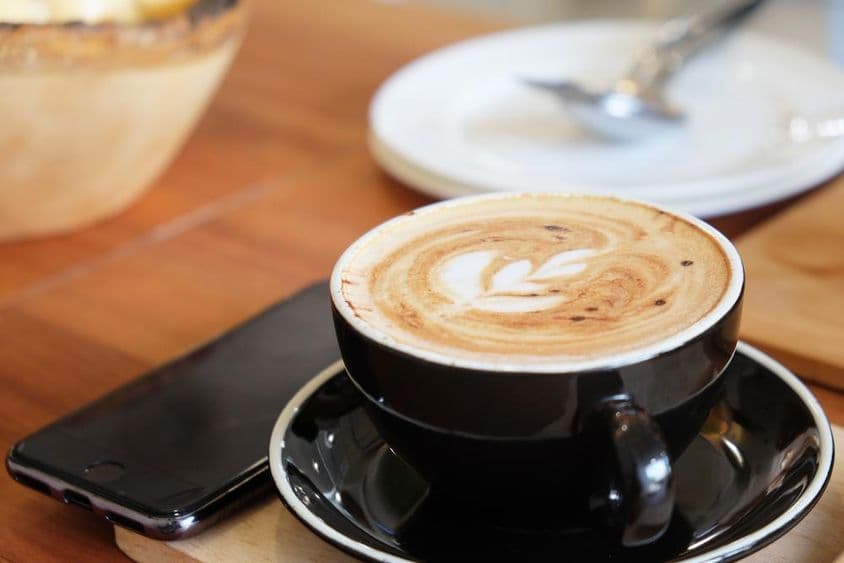 Šálka cappuccina na stole s telefónom vedľa nej.