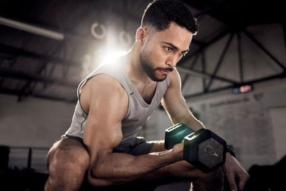 Svalnatý muž posilňuje bicepsy s malou činkou v posilňovni.