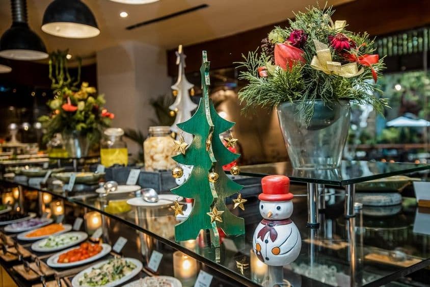 Malý snehuliak v reštaurácii na pulte so zeleninou, vedľa dreveného vianočného stromčeka.