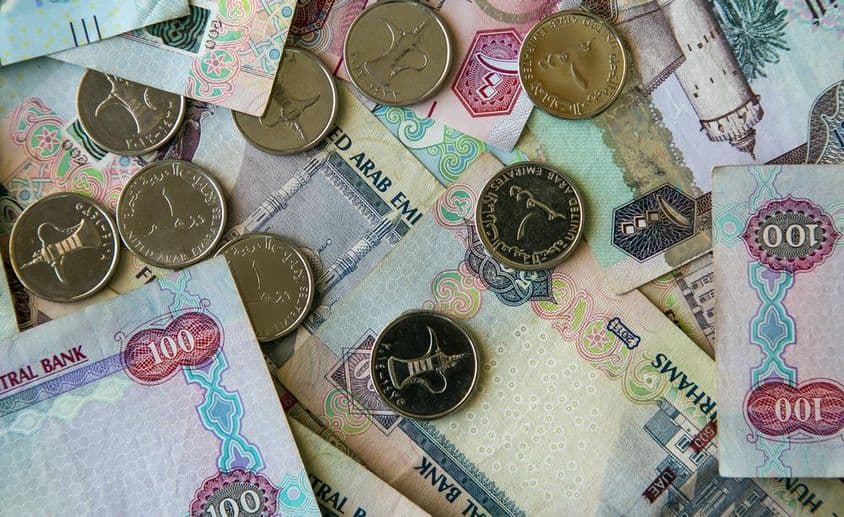 Dubai papierová mena roztrúsená na stole s 1 dirhamovými mincami hore.