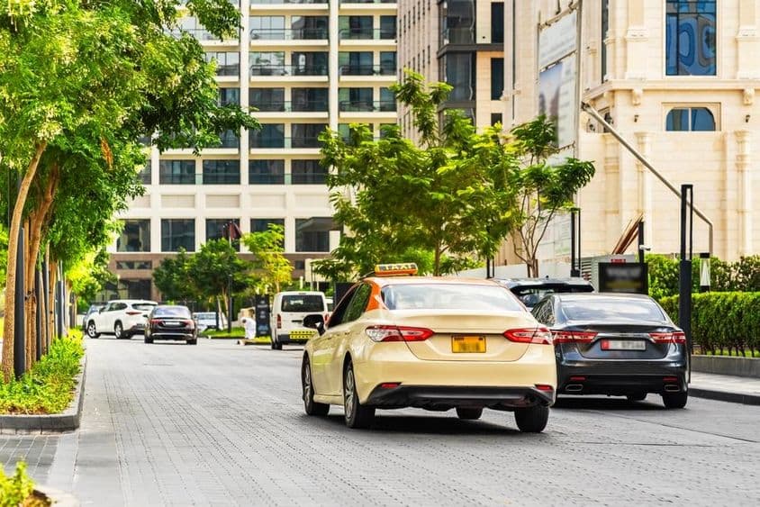 Autá na cestách v Dubaji, taxík v popredí, domy v pozadí.