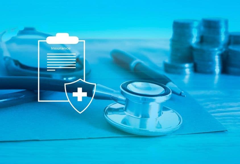 Zdravotné poistenie v popredí, stetoskop a drobné mince v pozadí.