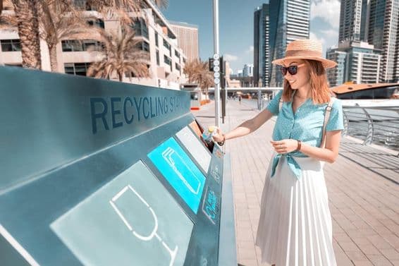 Vhadzovanie fľaše do recyklačného koša v Dubaji, s mrakodrapmi v pozadí.