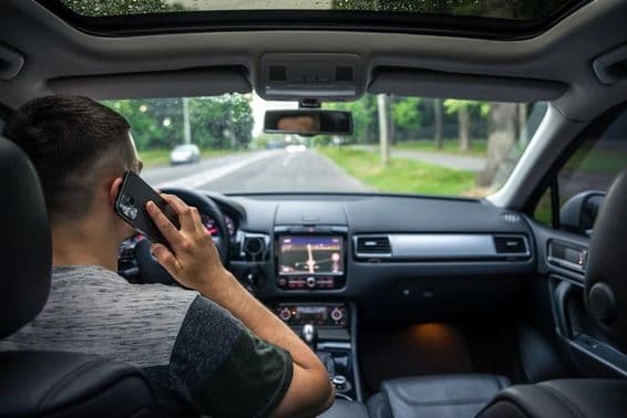 Mladý muž používa mobilný telefón počas šoférovania auta.