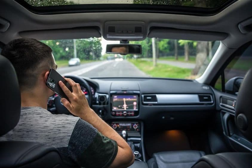 Mladý muž používa mobilný telefón počas šoférovania auta.