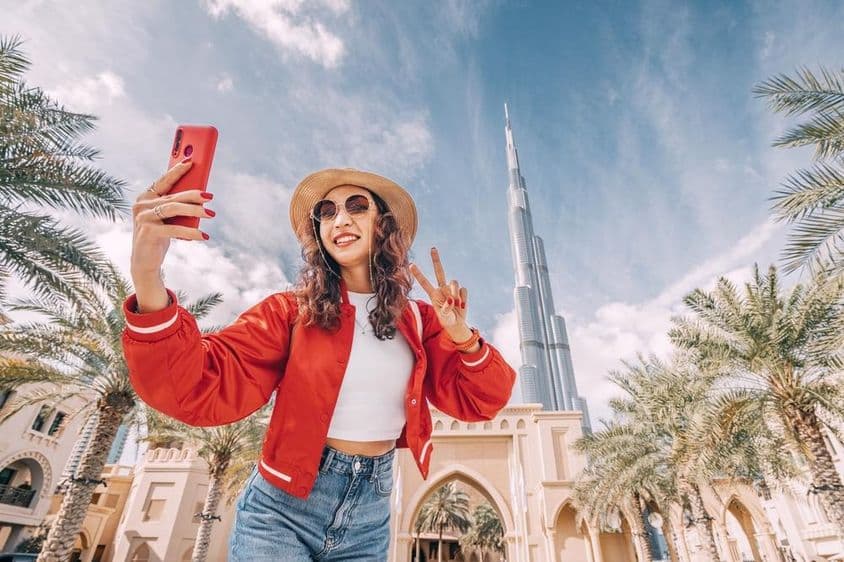 Mladá žena v červenom tope si robí selfie s Burj Khalifou v pozadí.