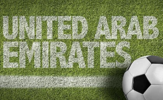 Nápis SAE namaľovaný na tráve s futbalovou loptou.