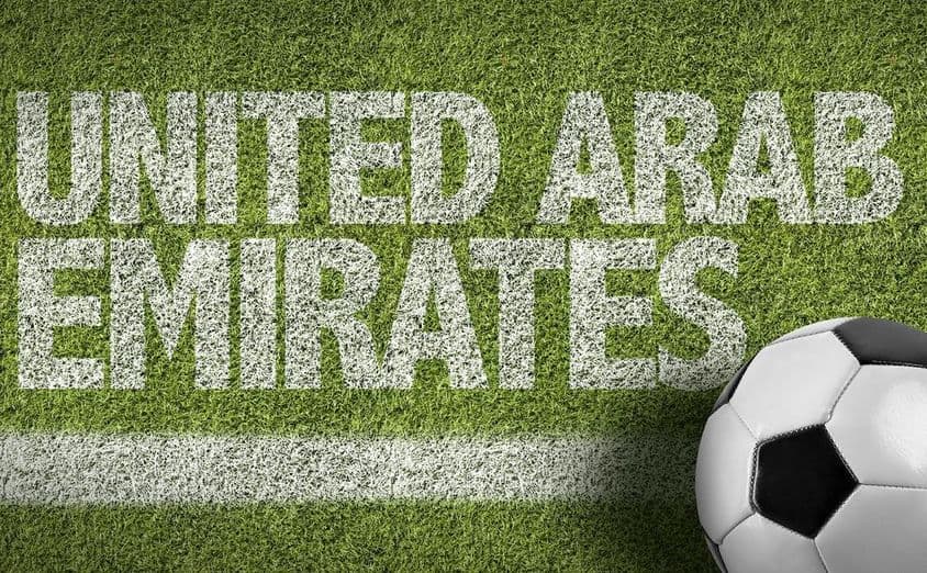 Nápis SAE namaľovaný na tráve s futbalovou loptou.