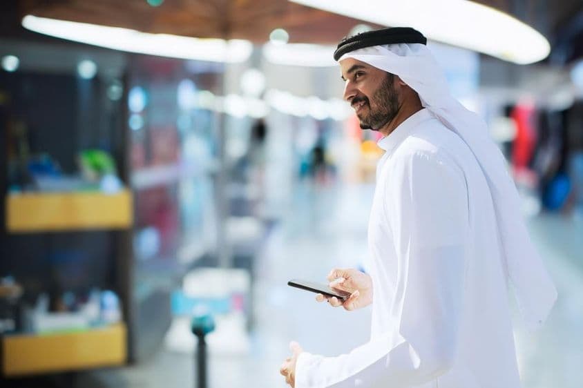 Arab muž na letisku v Dubaji držiaci telefón.
