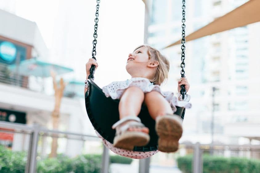 Šťastné malé dievčatko sa hojda v škôlkárskej záhrade.