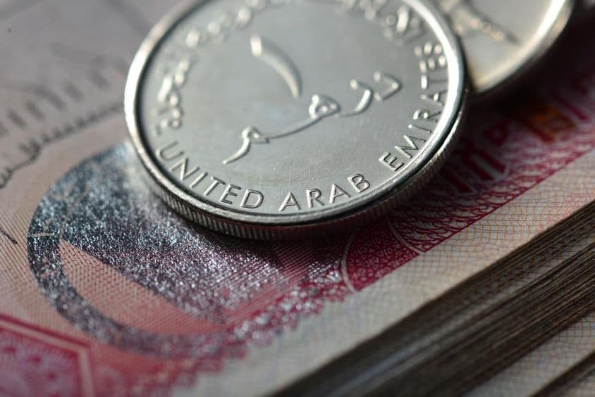 Kovová minca jeden dirham na kôpke bankoviek.