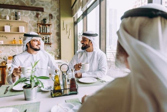 Traja podnikatelia pijú čaj v Dubaji, oblečení v tradičnom emirátskom odeve.