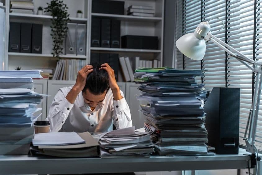 Kancelársky pracovník si drží hlavu kvôli preťaženiu prácou.