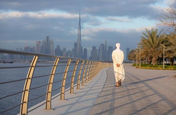 Emirátsky muž kráčajúci po chodníku s Burj Khalifou v pozadí.