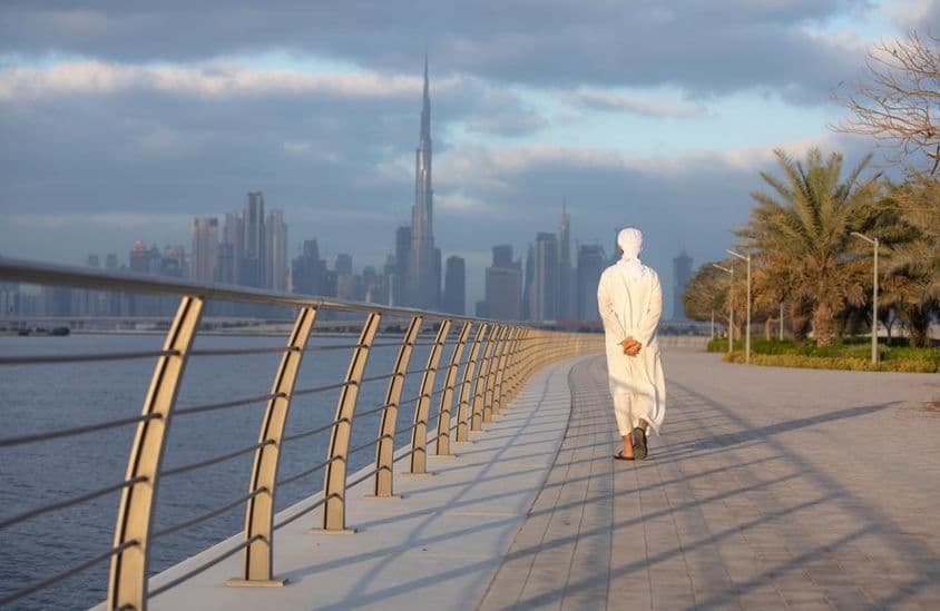 Emirátsky muž kráčajúci po chodníku s Burj Khalifou v pozadí.