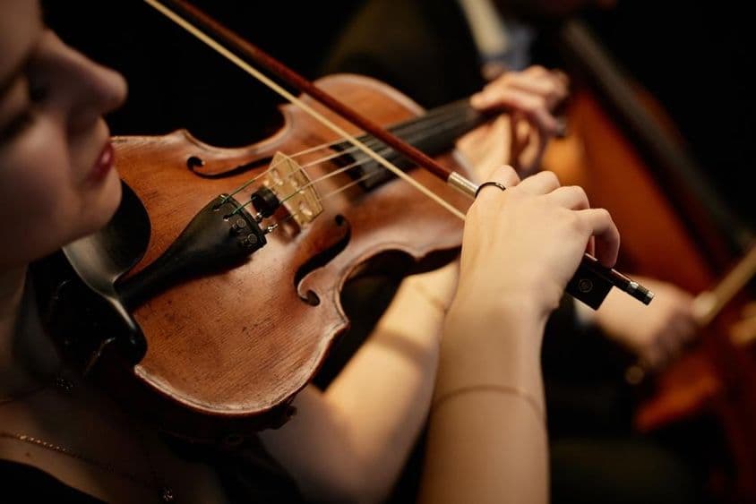Hudobníčka orchestru hrajúca na husle s obežníkom počas koncertu na pódiu.