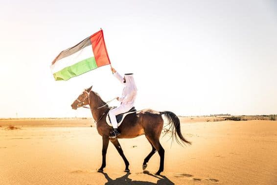 Muž zo Stredného východu v tradičnom emirátskom oblečení jazdiaci na arabskom koni v dubajskej púšti.