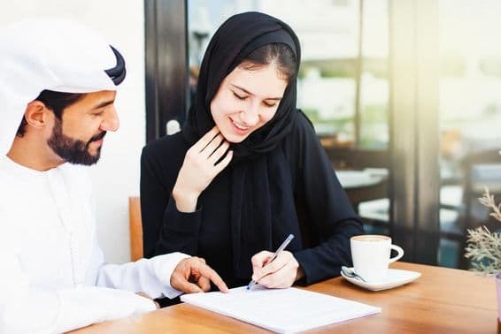 Arabský muž podávajúci dokumenty na podpis žene s hidžábom.